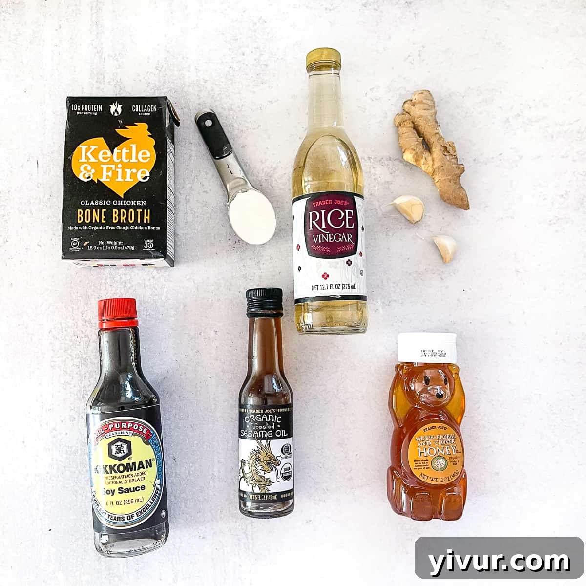 Overhead shot of stir fry sauce ingredients including soy sauce, broth, sesame oil, garlic, and ginger arranged on a white surface.