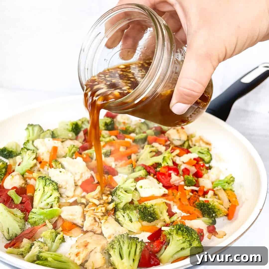 Pouring glossy stir fry sauce over chicken and vegetables in a skillet, showing thickness.