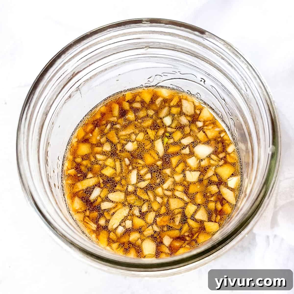Glass jar of dark stir fry sauce against a bright white background, with garlic pieces visible.