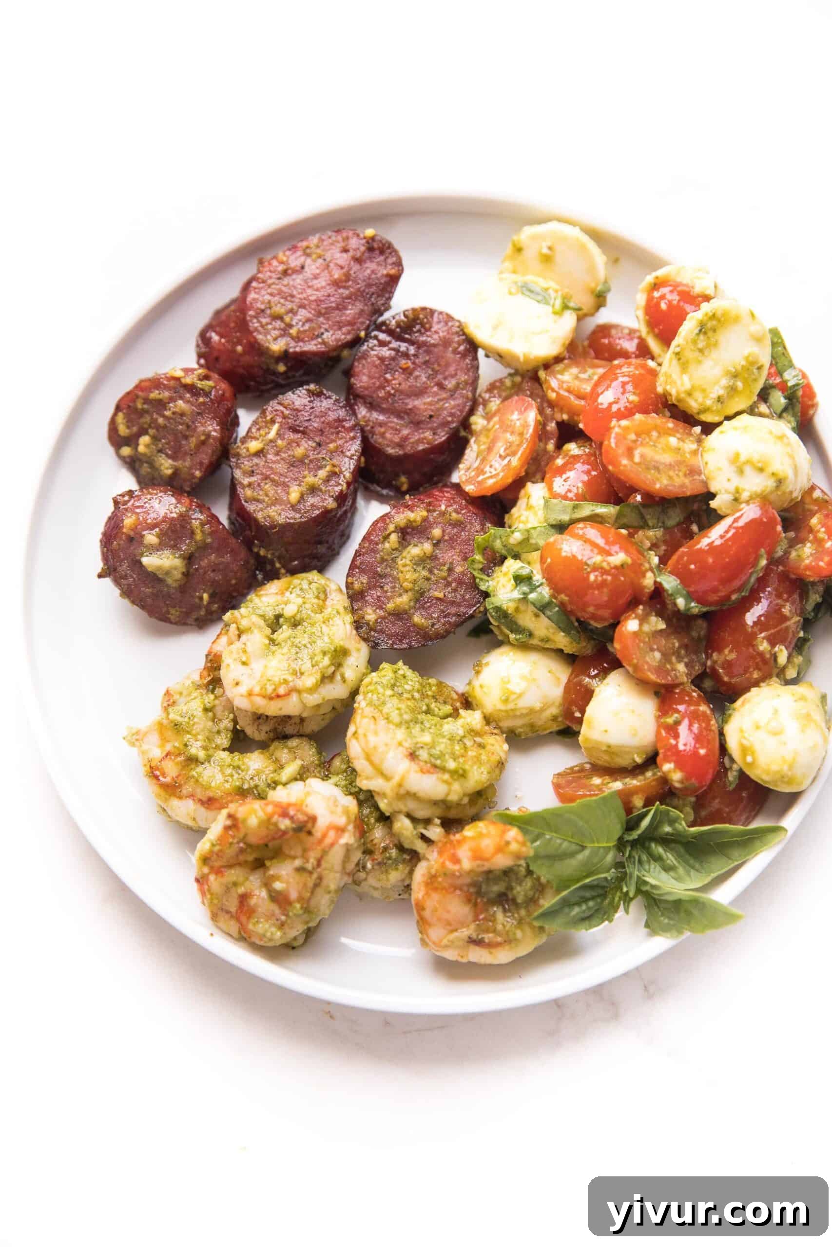 pesto shrimp, sausage and pesto caprese salad on a white plate