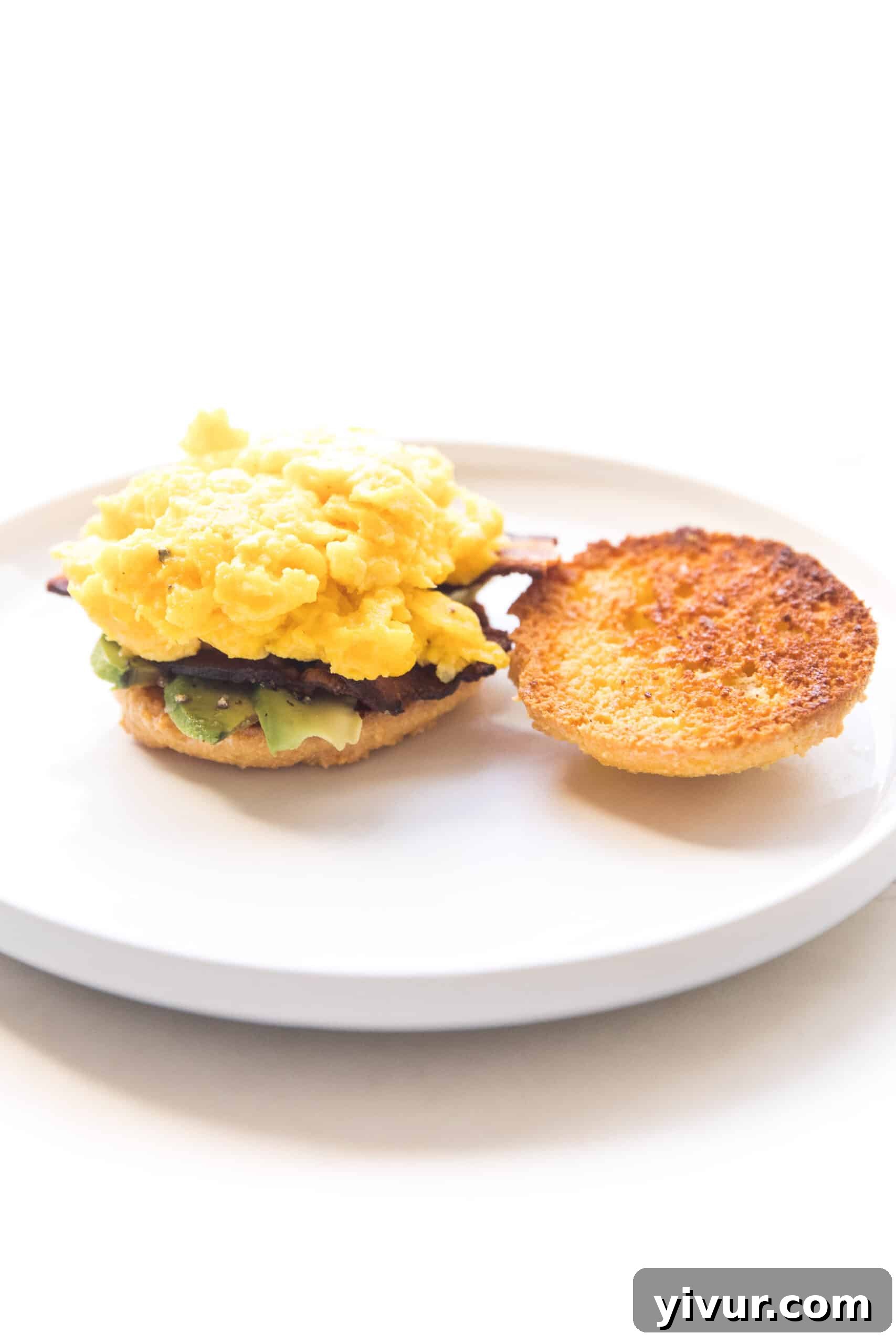 Another view of the keto biscuit breakfast sandwich on a white plate, highlighting the fresh, vibrant ingredients and the appealing texture of the biscuit. It suggests a gourmet yet simple homemade breakfast.