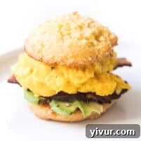 keto biscuit breakfast sandwich with egg, bacon and avocado on a white plate and background