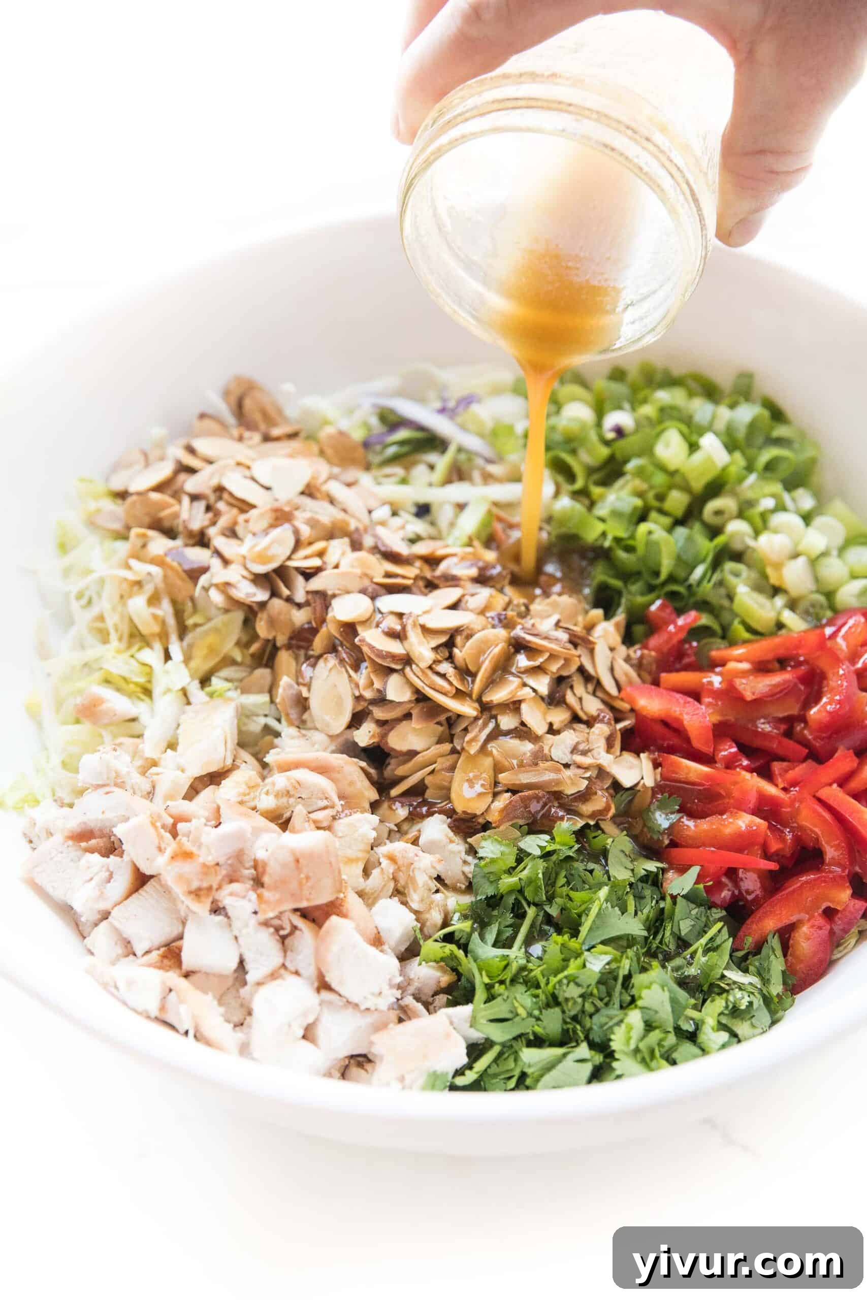 homemade asian dressing being poured over chinese chicken salad in a white bowl