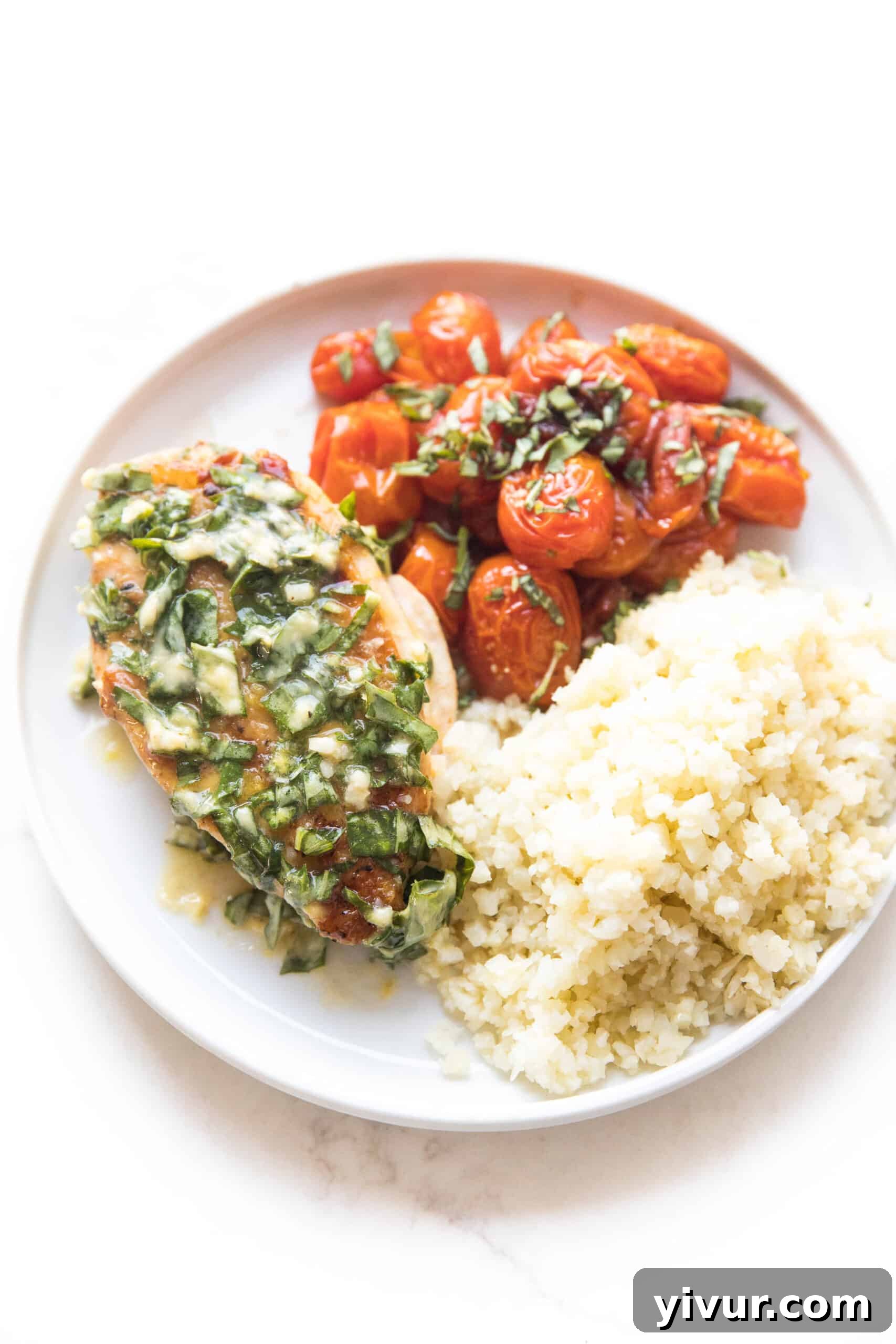 Crispy skin chicken with basil butter, blistered tomatoes and cauliflower rice on a white plate, ready to be served for a healthy keto dinner.