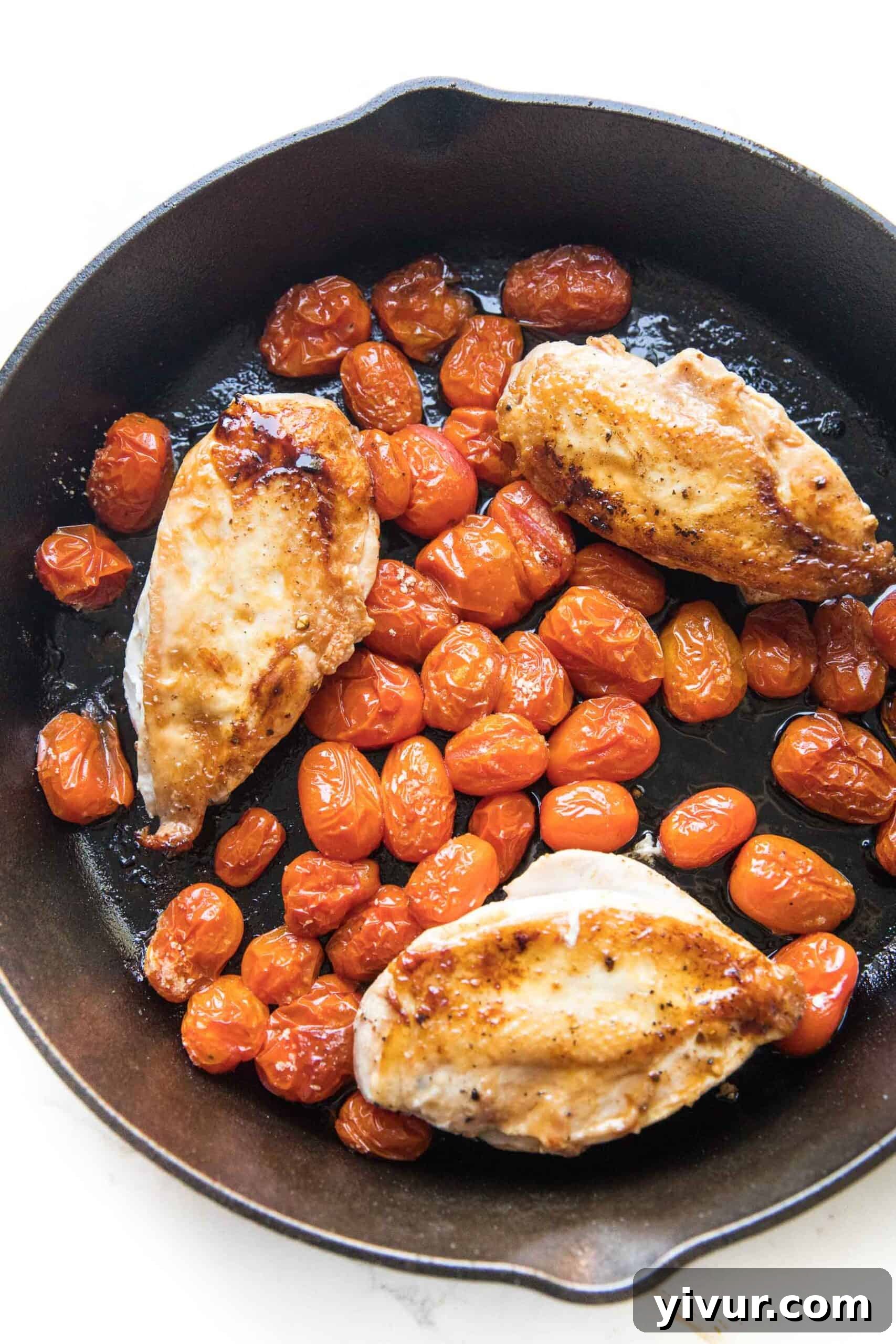 Close-up of cast iron skillet filled with golden brown skillet chicken and perfectly blistered grape tomatoes, fresh off the grill or out of the oven.