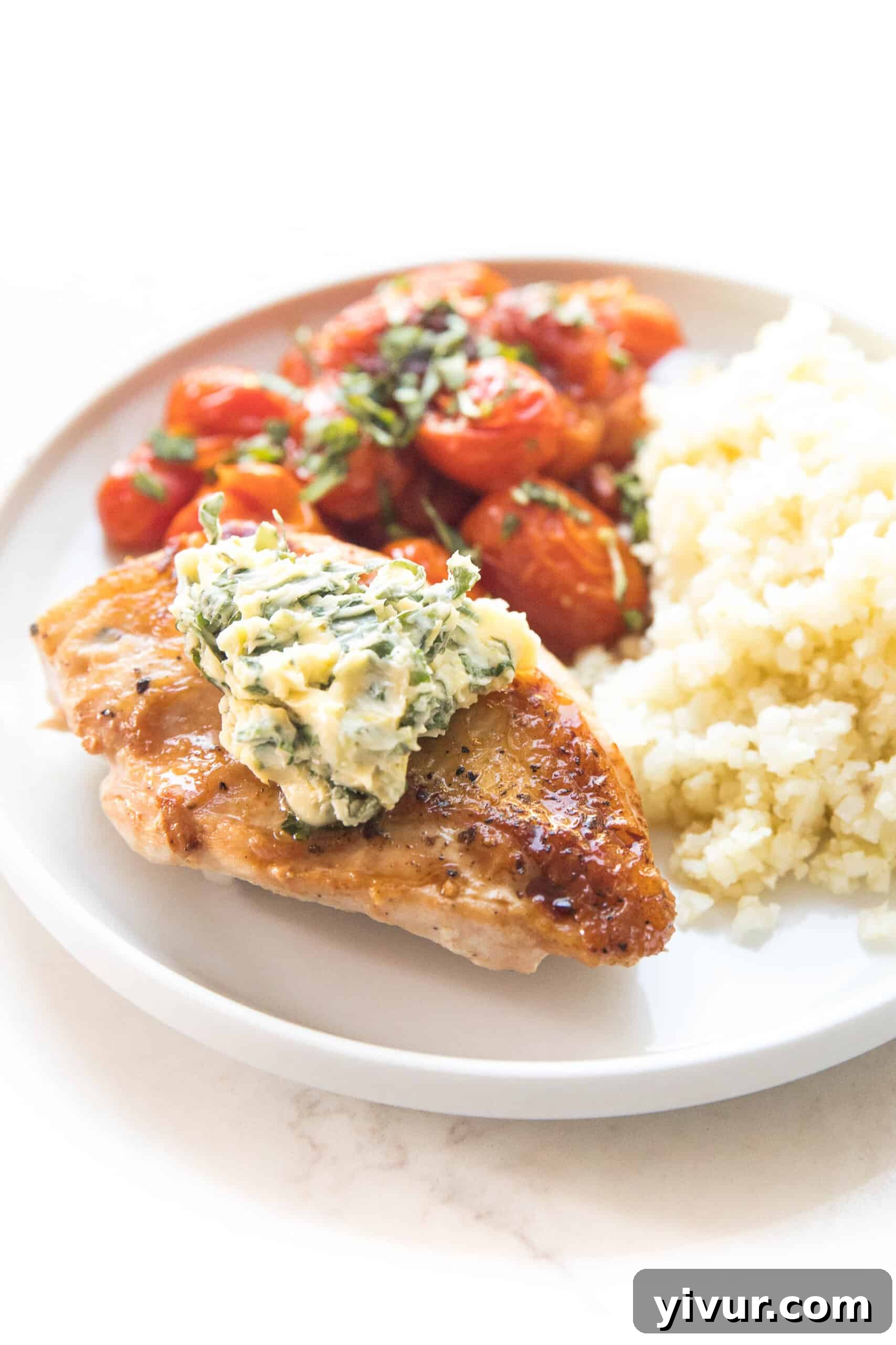 A serving of keto skillet chicken, blistered tomatoes, and a dollop of basil butter, accompanied by fluffy cauliflower rice for a complete meal.
