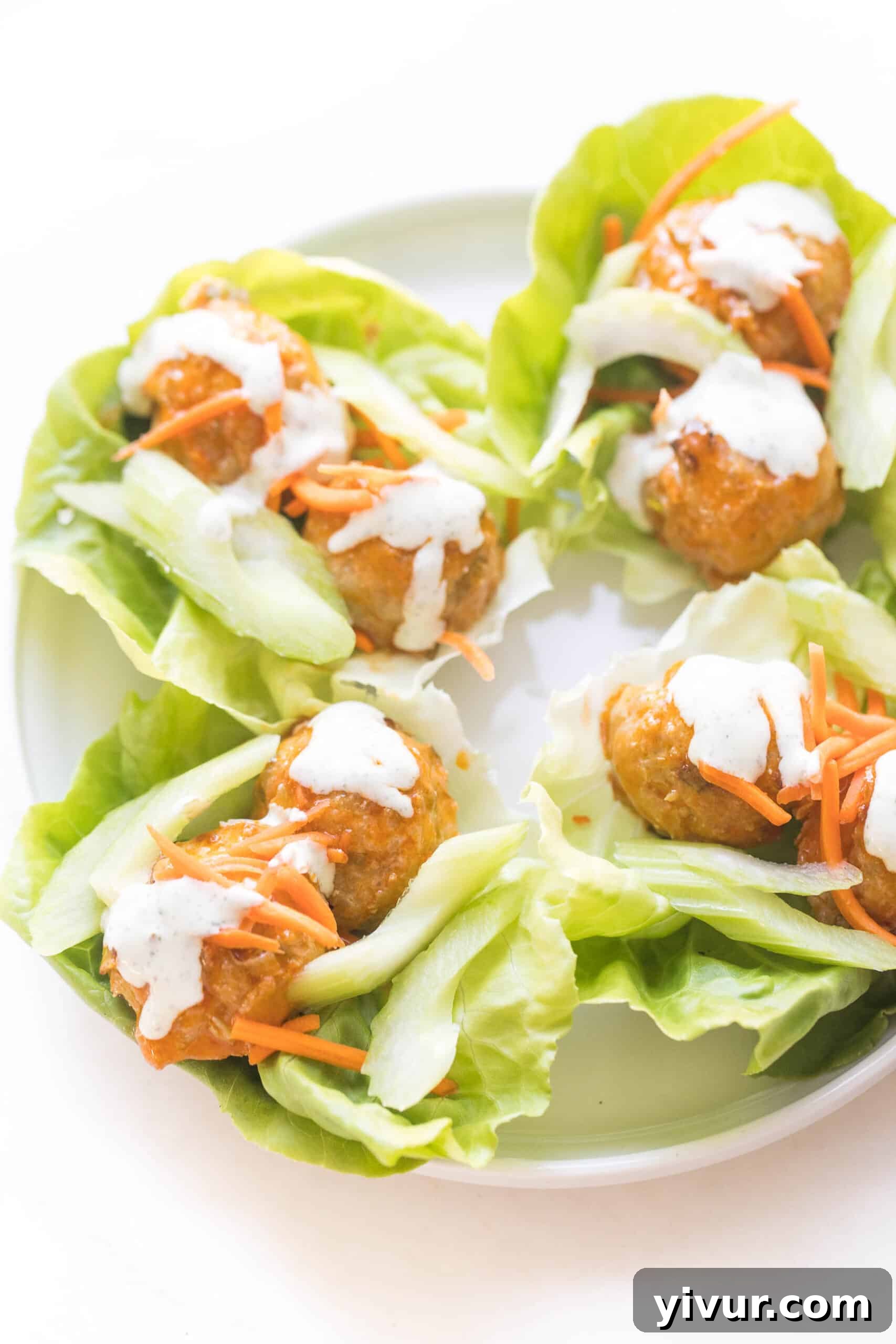 keto buffalo turkey meatballs on lettuce wraps topped with ranch dressing on a white plate and background