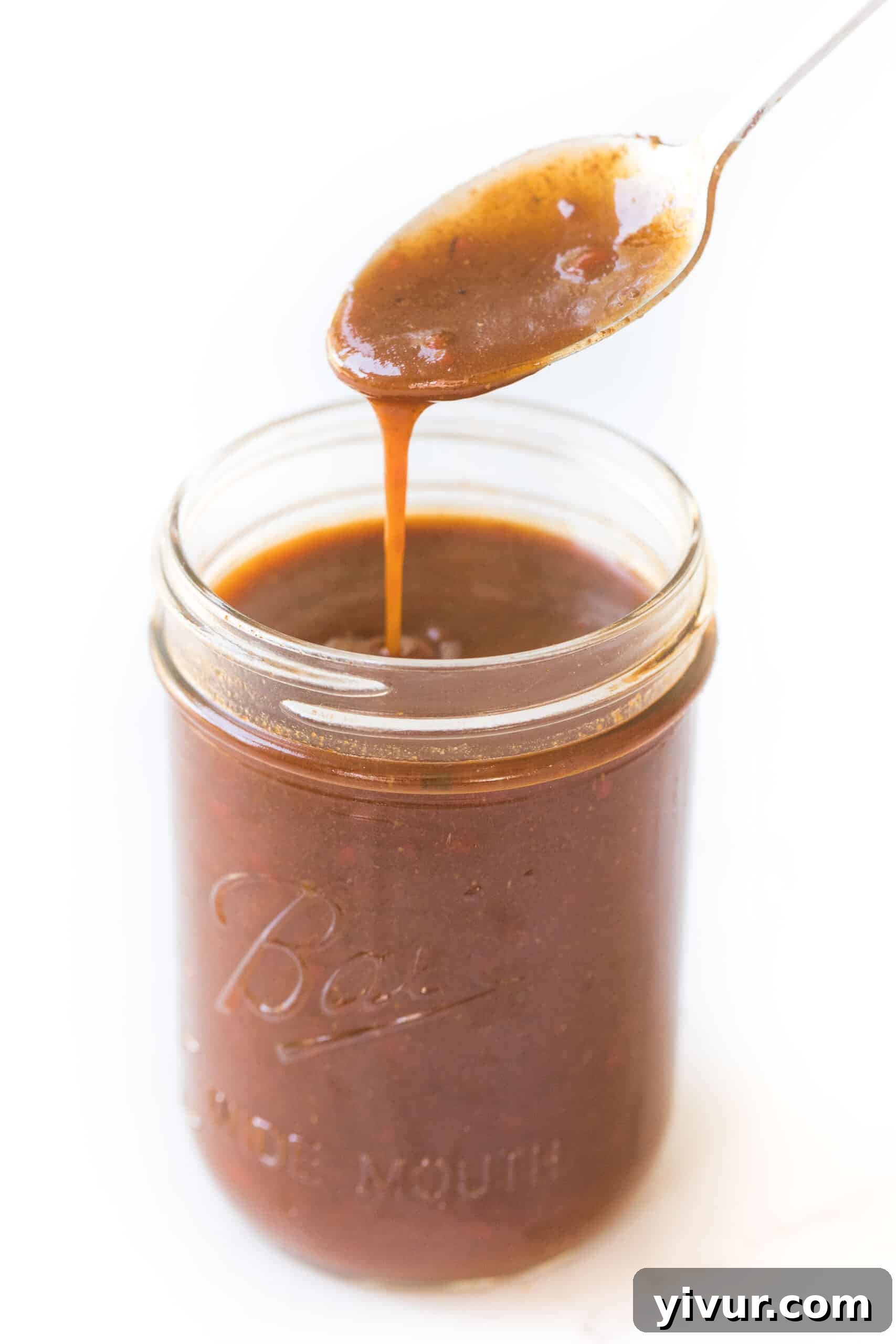 spoon in a mason jar of homemade red enchilada sauce on a white background