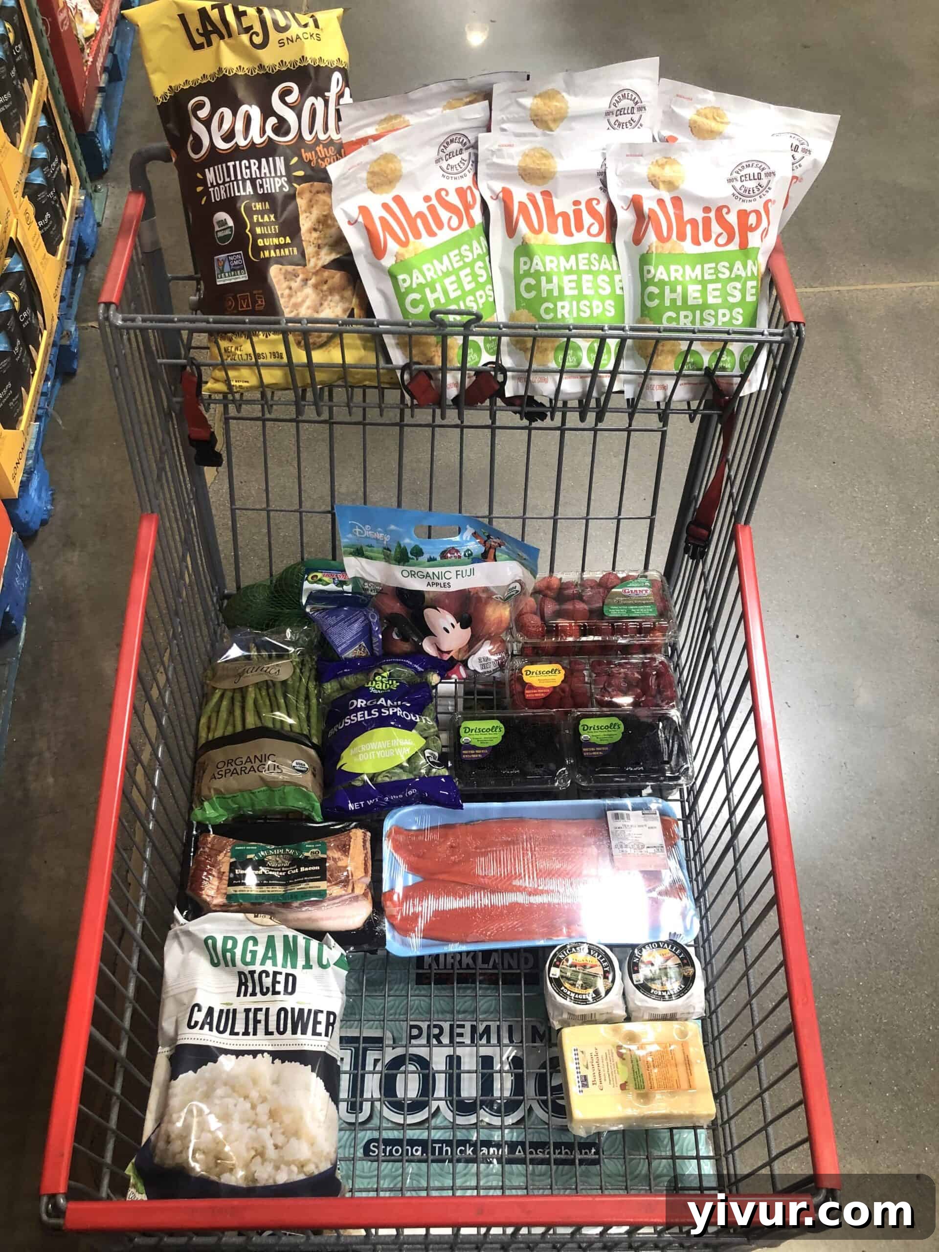 A large grocery haul from Costco, featuring bulk organic produce, essential pantry items, and various healthy snacks, laid out on a kitchen counter.