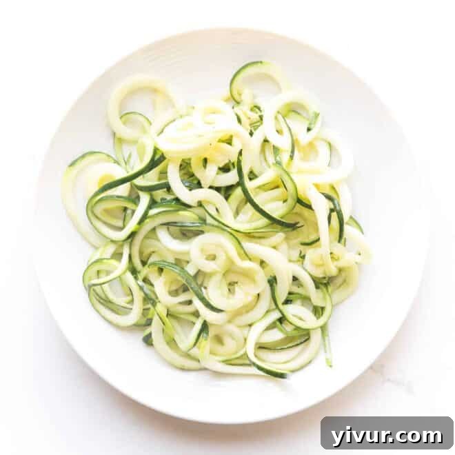 Freshly spiralized zucchini noodles on a white plate, ready for a low-carb pasta alternative.