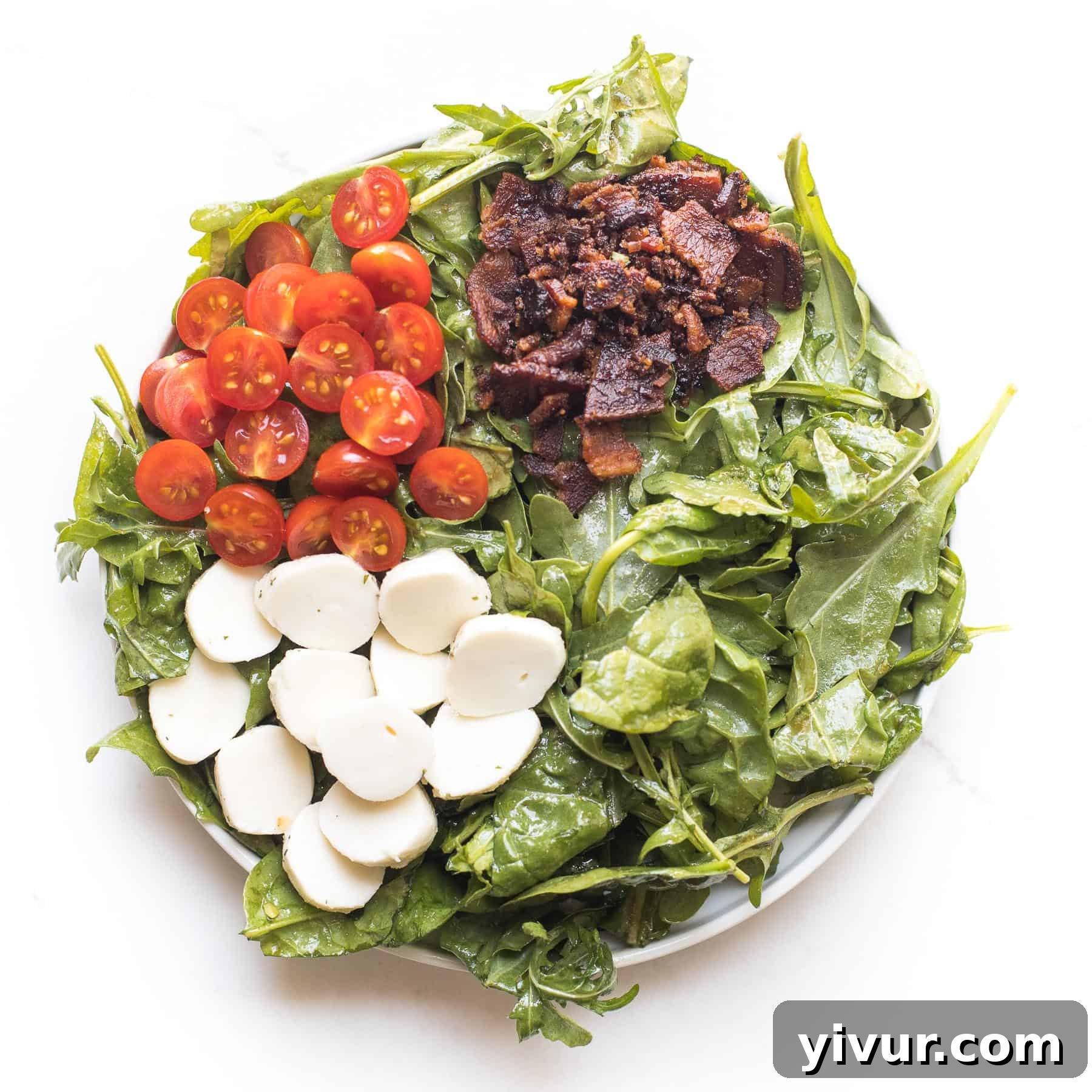 keto salad with bacon, tomatoes and mozzarella cheese on spinach and arugula on a white plate