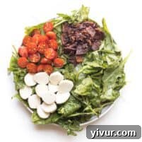 keto salad with bacon, tomatoes and mozzarella cheese on spinach and arugula on a white plate