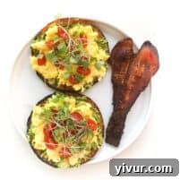 keto avocado toast topped with egg, tomatoes, microgreens and bacon on a white plate and background