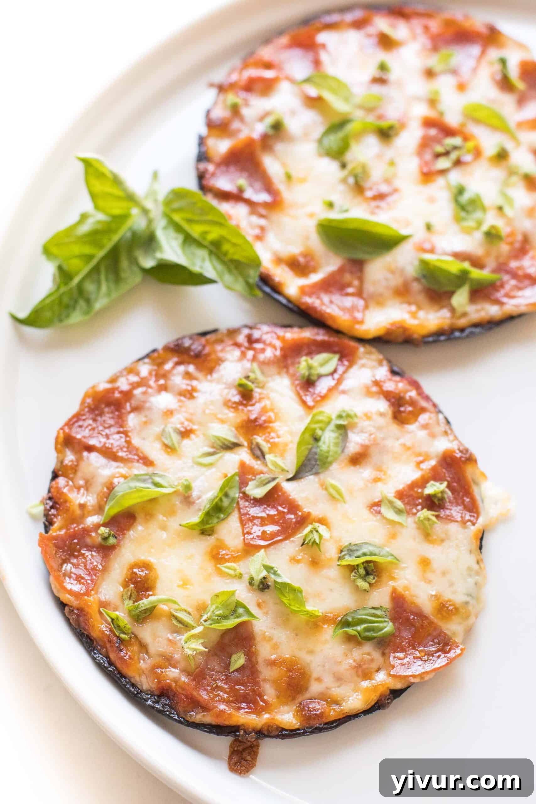 Two keto mini cauliflower thin pepperoni pizzas on a white plate topped with fresh basil, ready to eat.