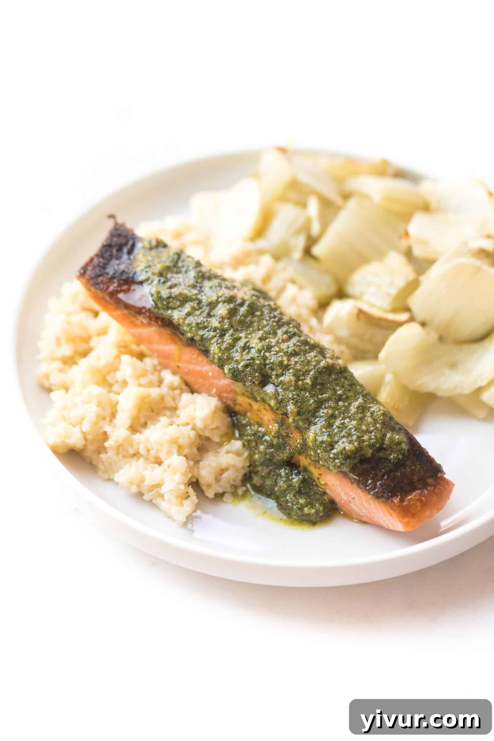 salmon topped with a green sauce on a white plate and background