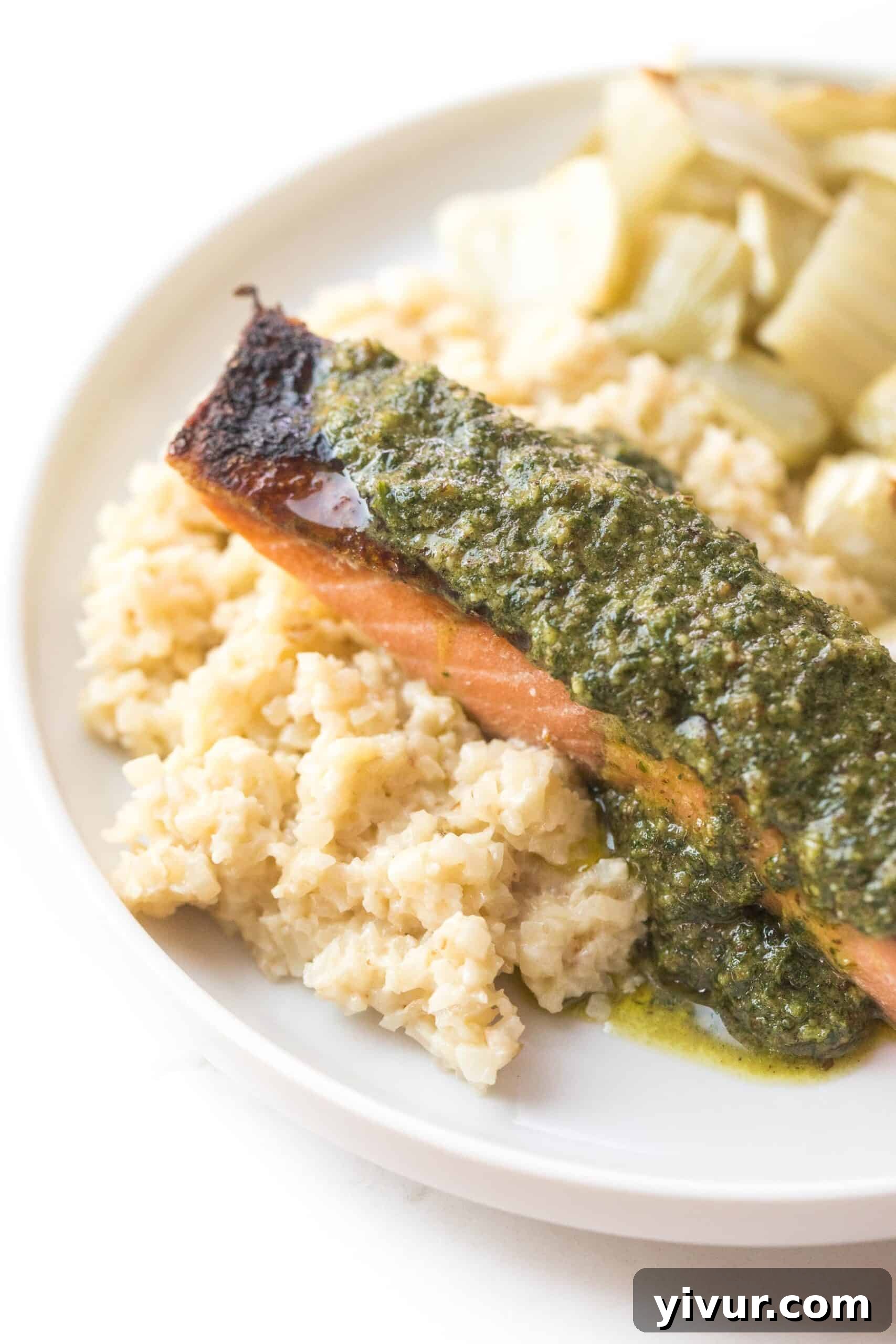 salmon topped with a green sauce on a white plate and background