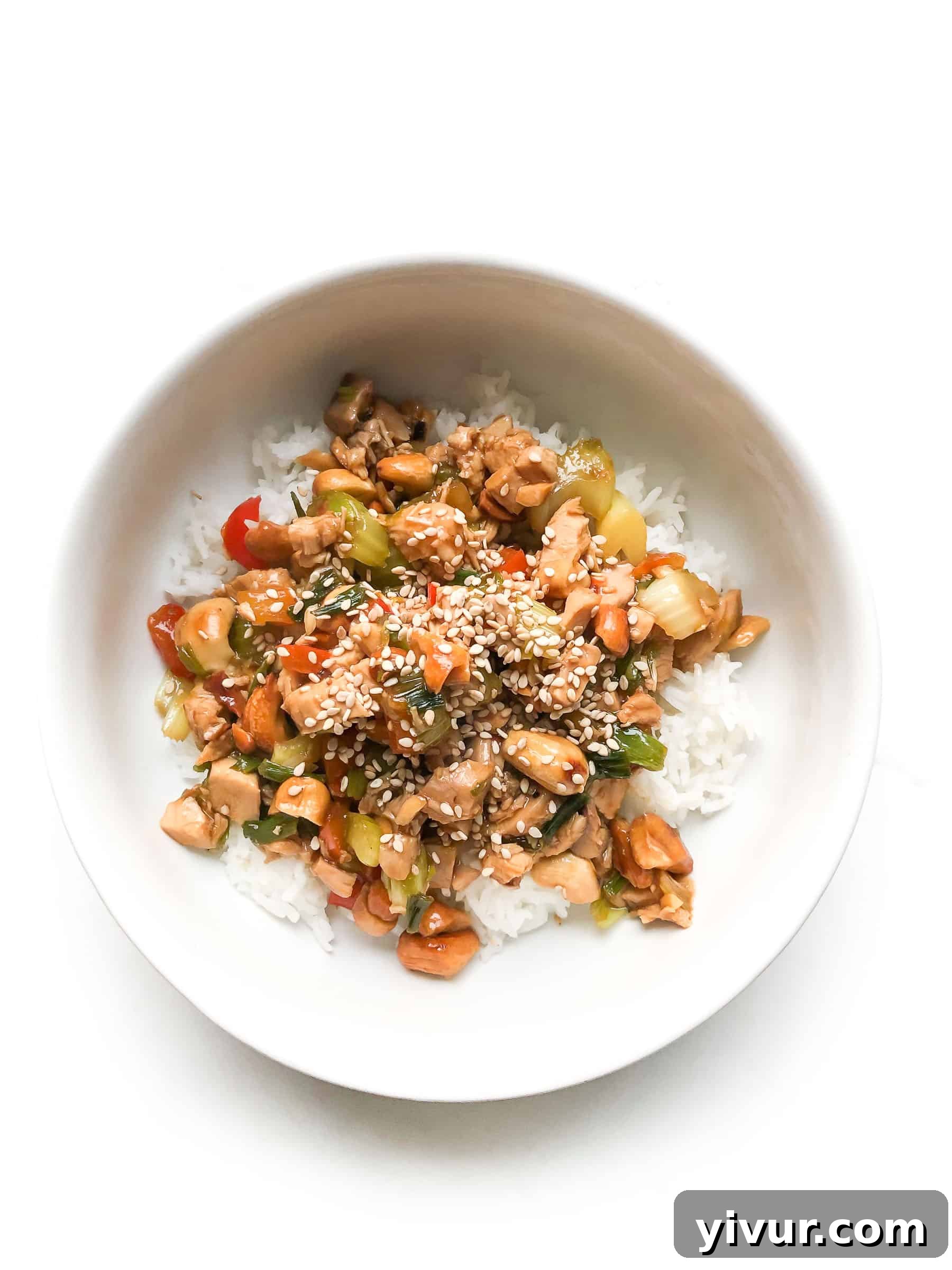 CHICKEN AND CELERY STIR FRY IN A WHITE BOWL TOPPED WITH SESAME SEEDS OVER CAULIFLOWER RICE