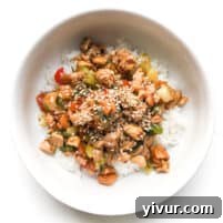 CHICKEN AND CELERY STIR FRY IN A WHITE BOWL TOPPED WITH SESAME SEEDS OVER CAULIFLOWER RICE IN A WHITE BOWL AND BACKGROUND