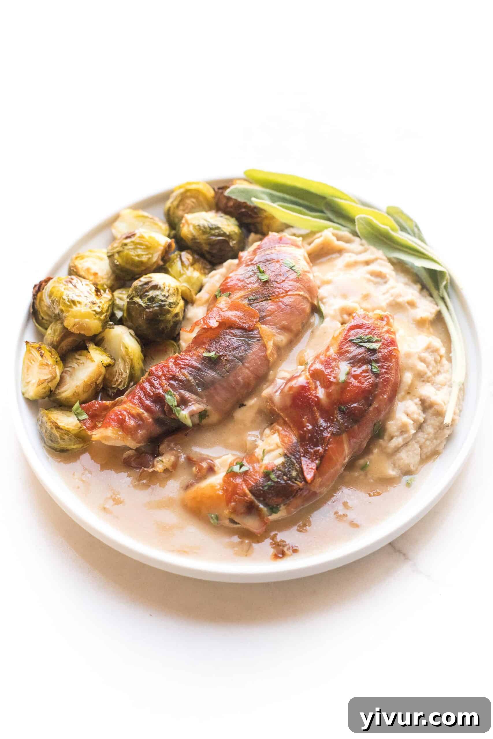 keto + whole30 prosciutto wrapped chicken with creamy apple cider gravy over mashed cauliflower with roasted brussels sprouts on a white plate and background