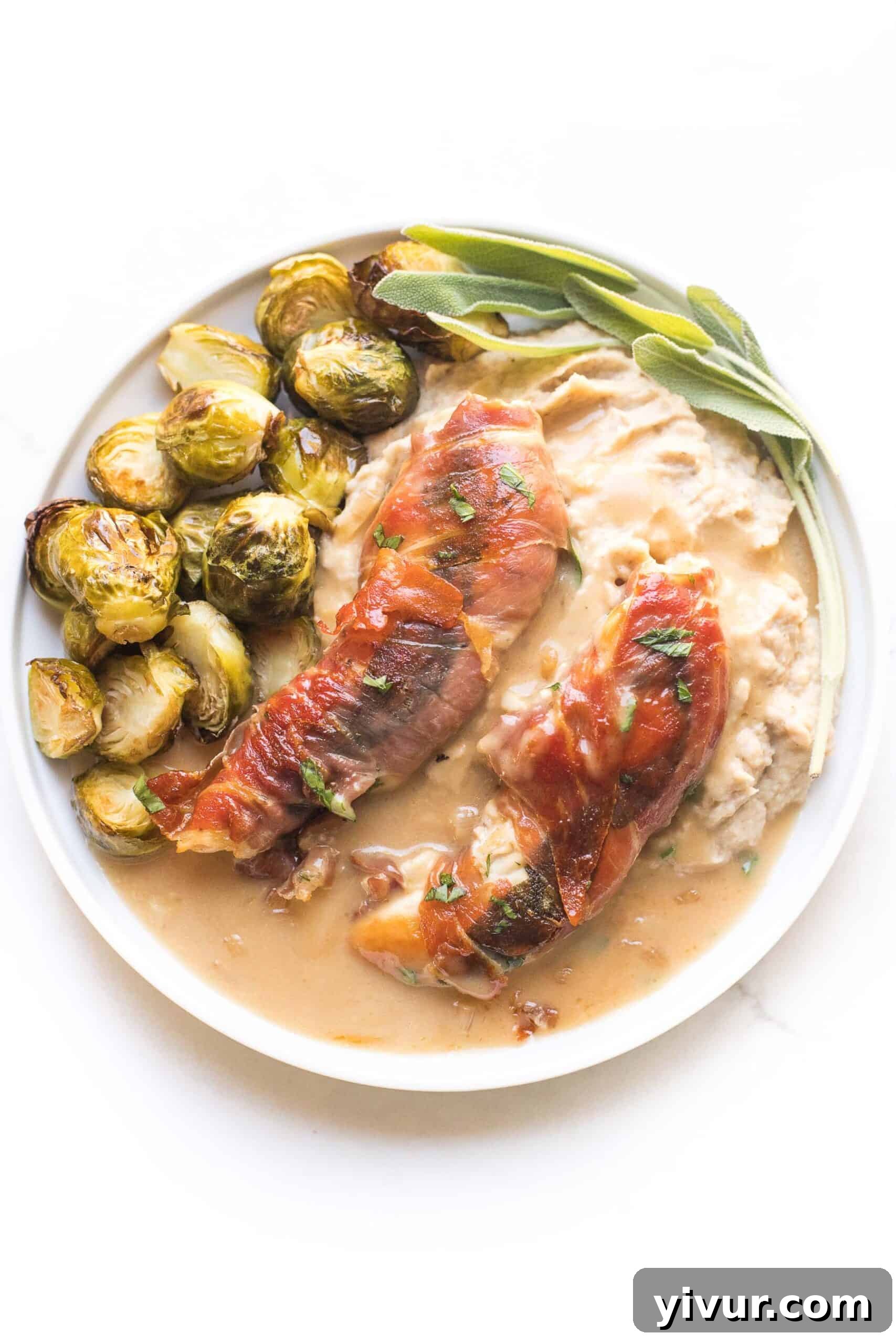 keto + whole30 prosciutto wrapped chicken with creamy apple cider gravy over mashed cauliflower with roasted brussels sprouts on a white plate and background