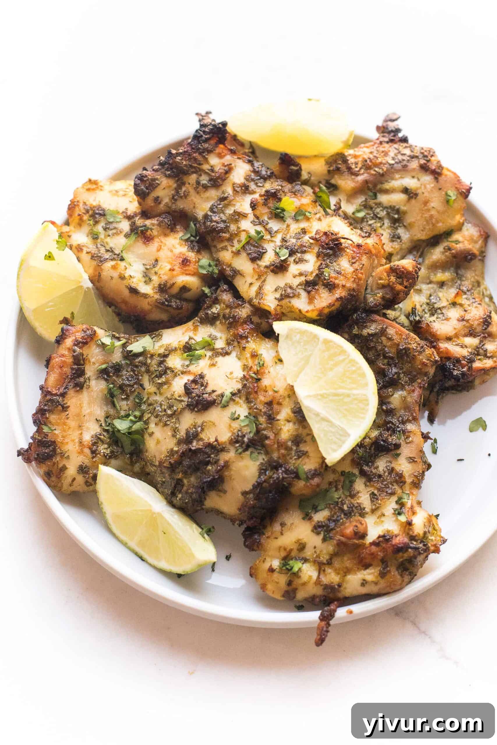 Perfectly roasted Whole30 + Keto Cilantro Lime Chicken Thighs arranged neatly on a white plate, garnished with fresh cilantro and lime wedges, showcasing their crispy, caramelized edges.