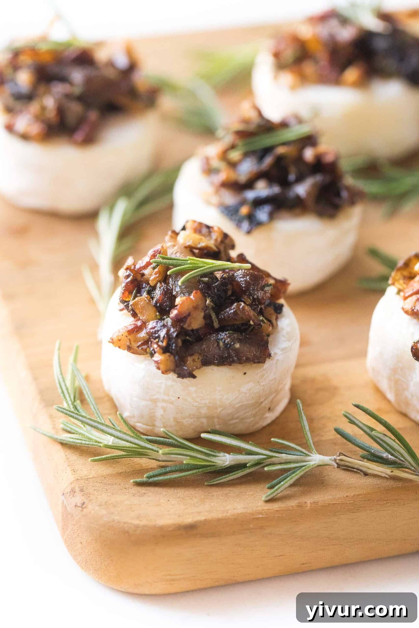 Brie cheese bites topped with caramelized onions, rosemary and pecan mixture on a cheese board, ready to serve.