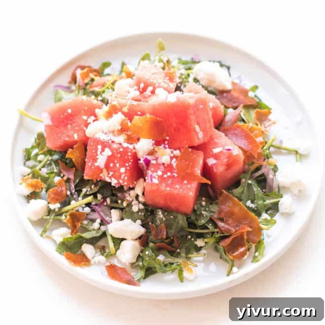 A refreshing Watermelon Feta Salad with Arugula, Crispy Prosciutto, and Red Onion on a white plate.