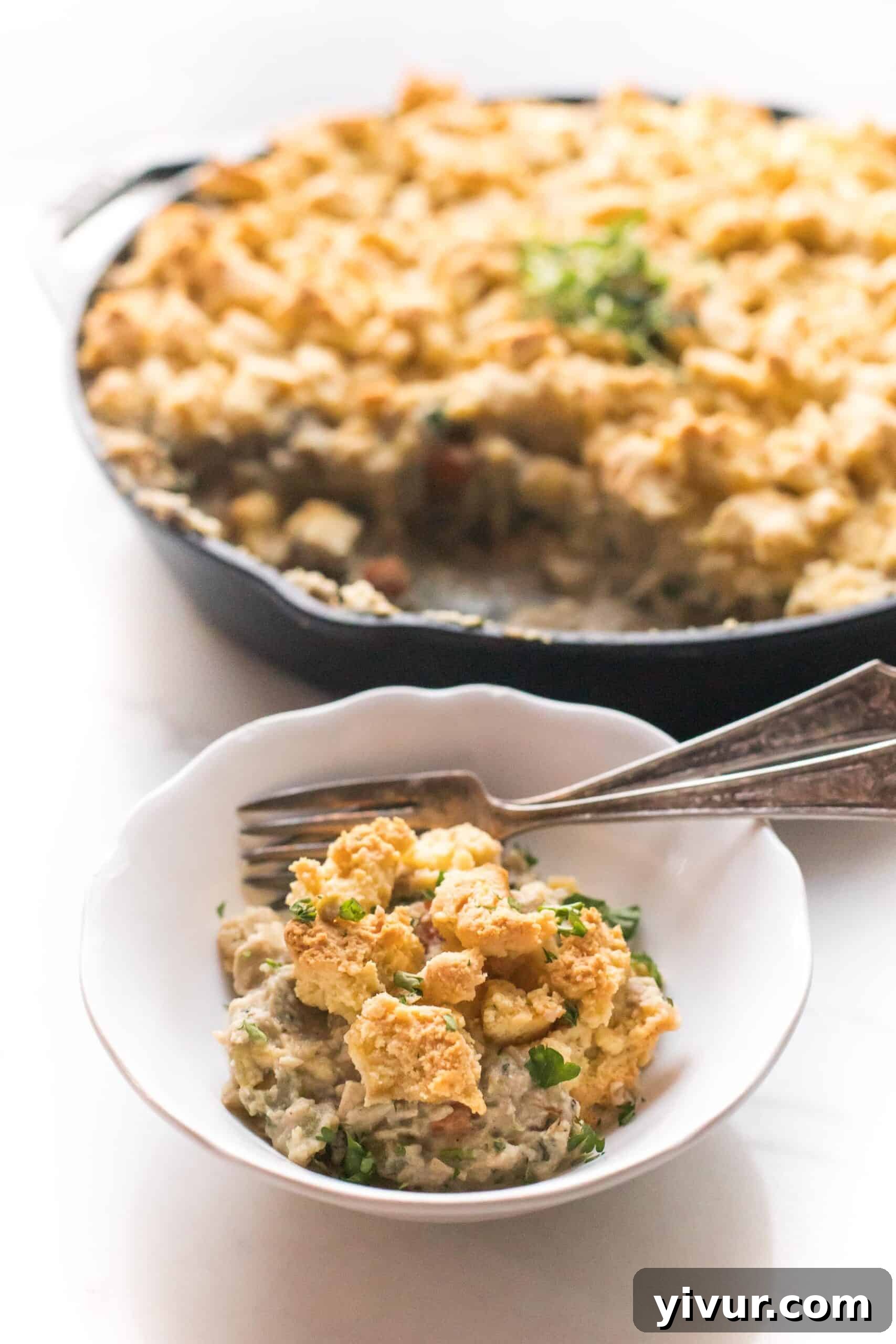 Close-up of Keto Chicken Pot Pie Crumble in a cast iron skillet with a serving in a white bowl, highlighting its creamy filling and golden biscuit topping