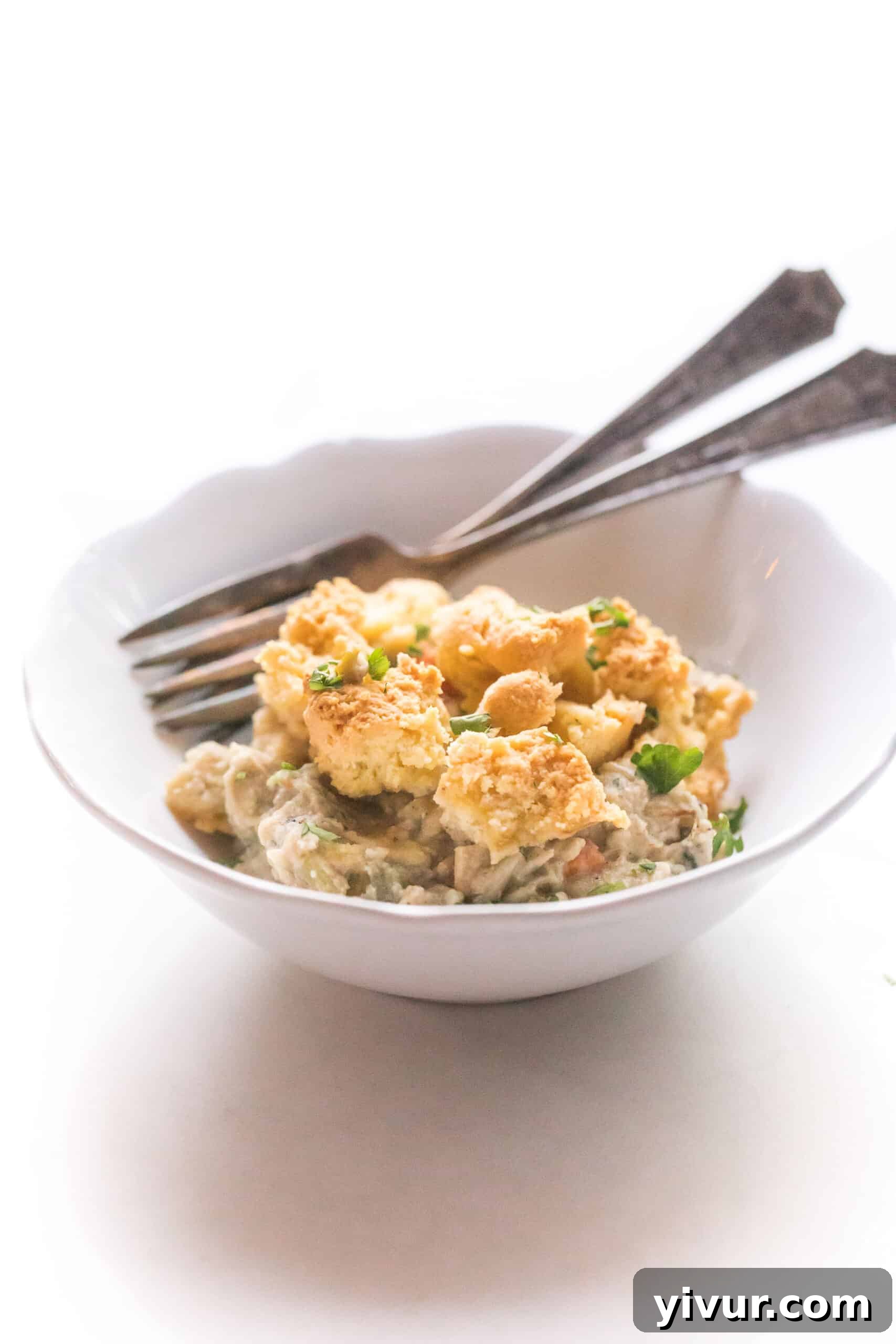 A serving of Keto Chicken Pot Pie Crumble in a white bowl, showcasing the golden biscuit topping and creamy filling