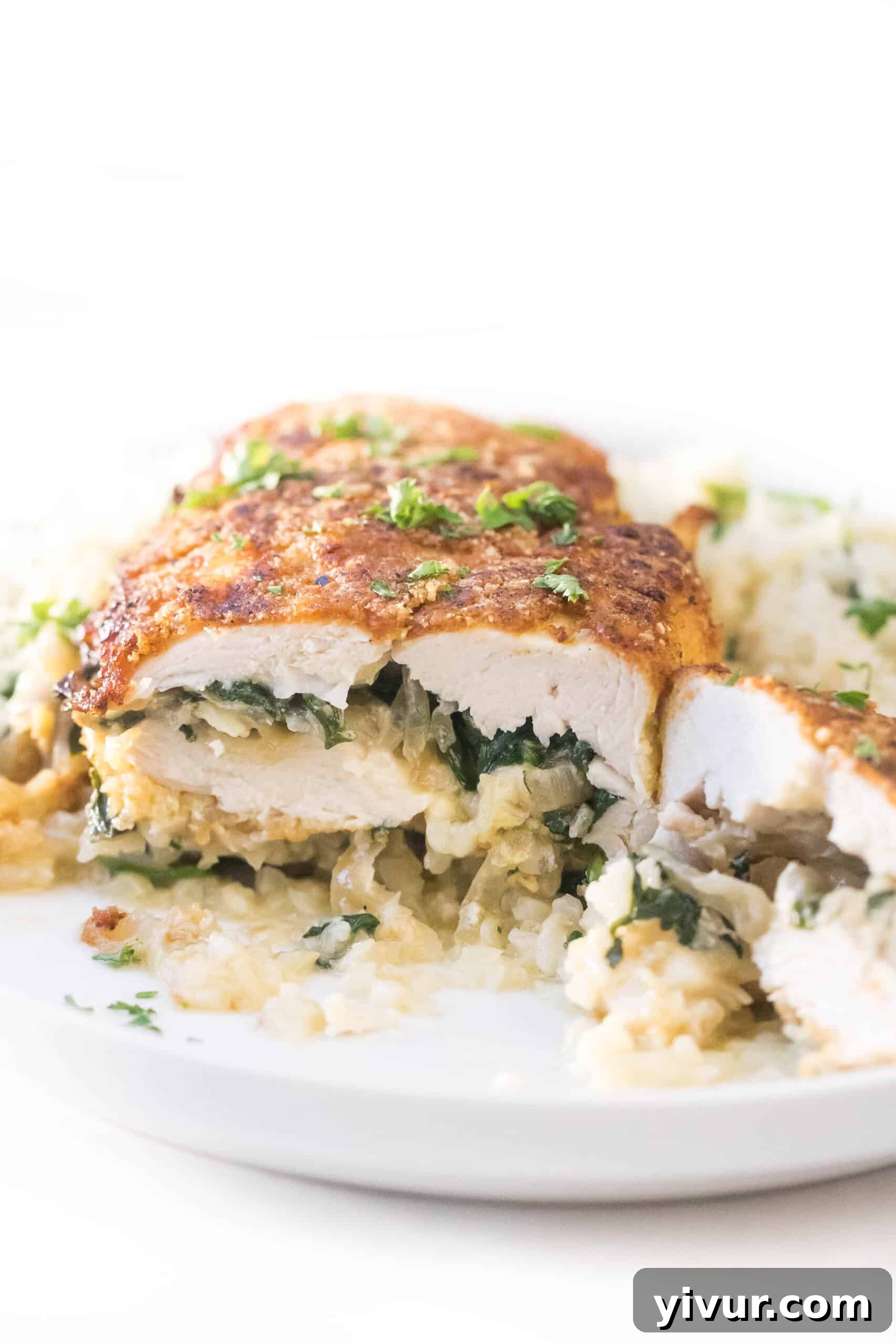keto brie + spinach stuffed chicken breast cut in half on a white plate with cauliflower rice