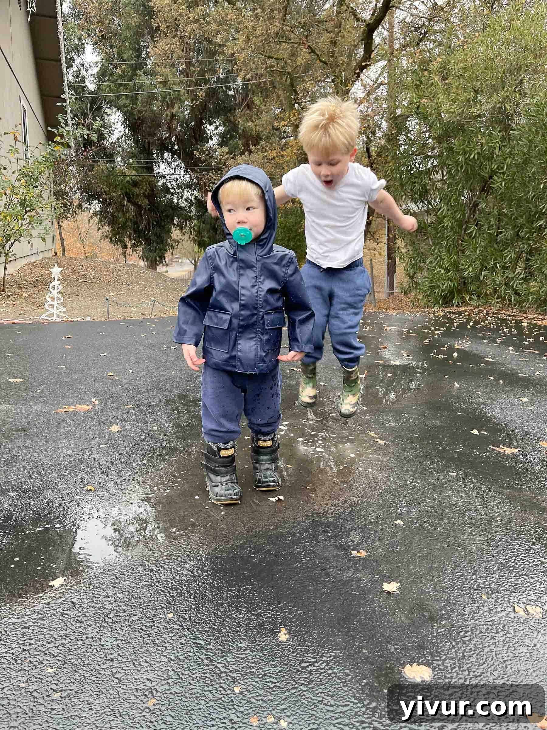 Two young boys in rain boots jumping in puddles on a rainy morning