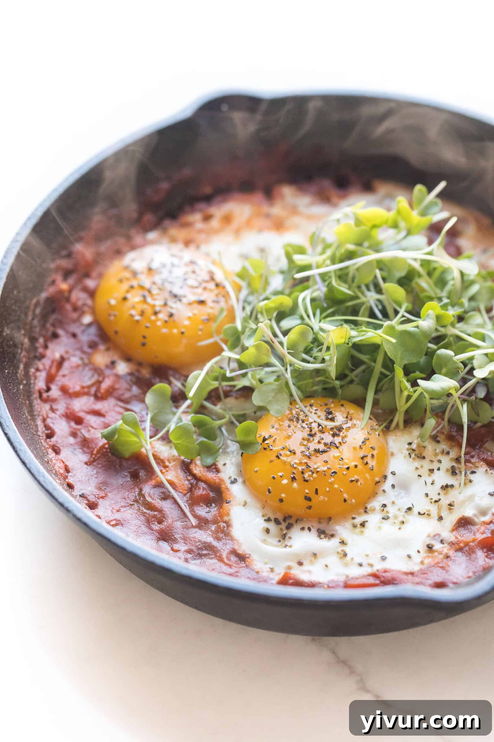 Keto Shakshuka: Flavorful Eggs in Robust Tomato Sauce 2 KETO SHAKSHUKA EGGS IN TOMATO SAUCE IN A CAST IRON SKILLET ON A WHITE BACKGROUND TOPPED WITH GREENS
