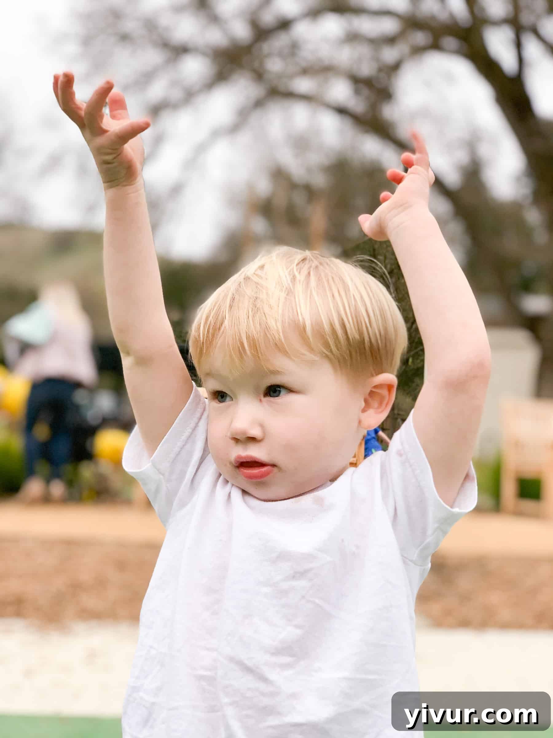 Son Ryan feeling for raindrops with his hand out during a light sprinkle at the playground, showing innocent wonder