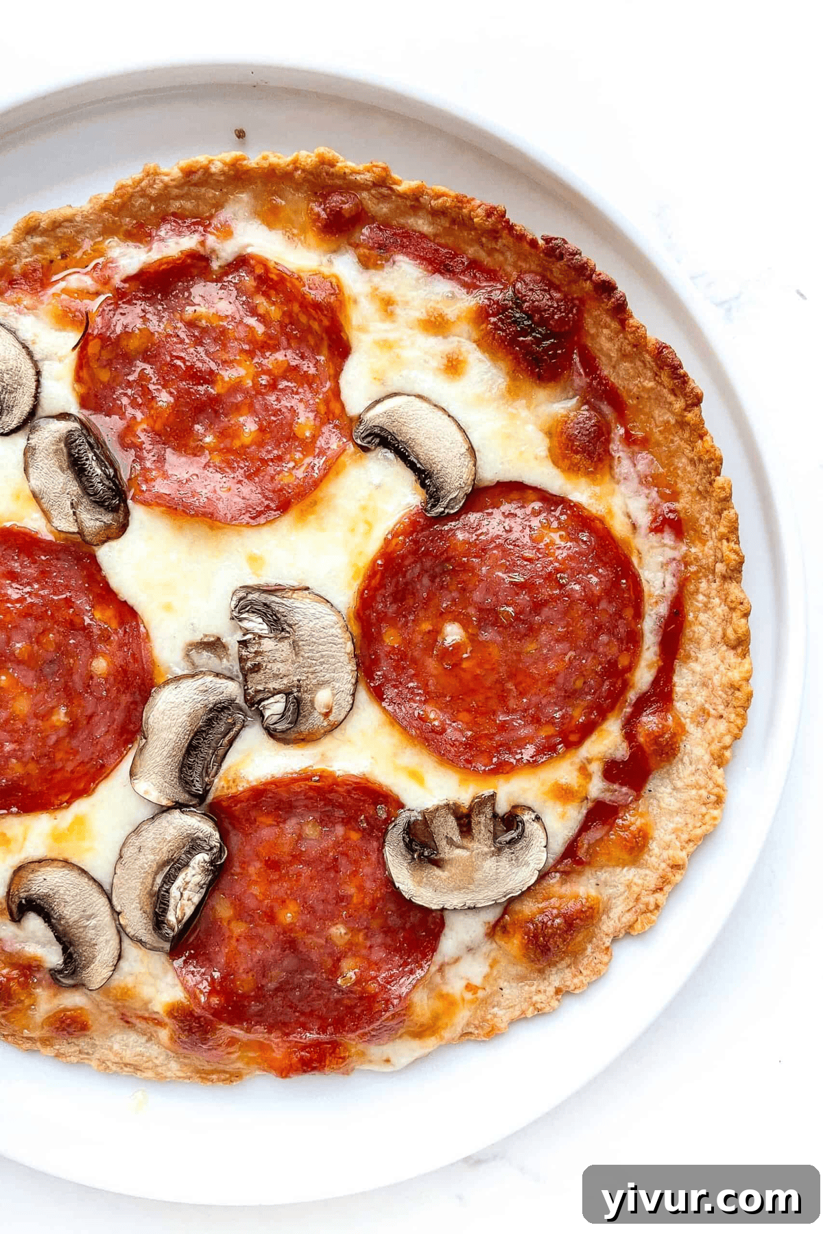 Close-up photo of a finished zero carb pizza with pepperoni and mushroom on a white plate