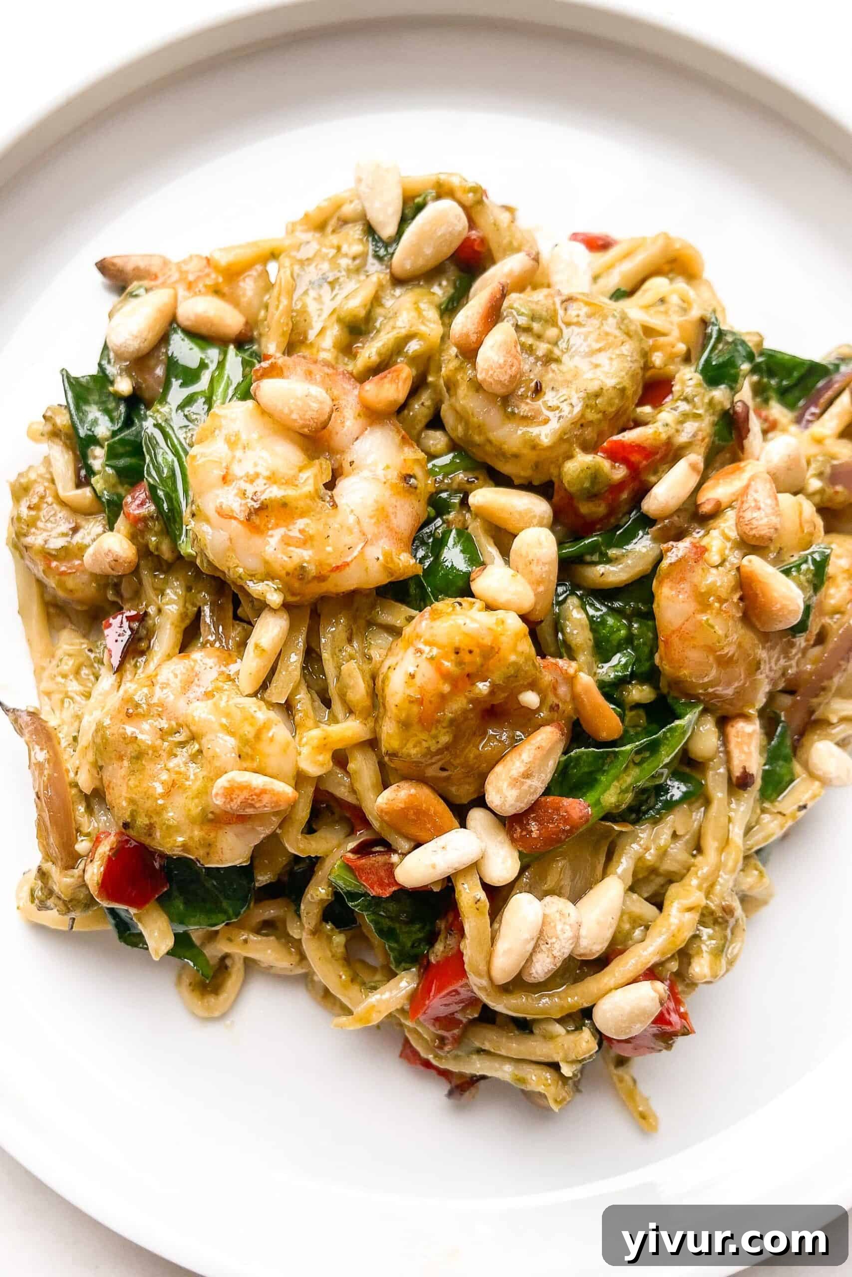 A vibrant plate of keto creamy pesto shrimp pasta, garnished with fresh herbs and a sprinkle of cheese, invitingly presented on a white plate.