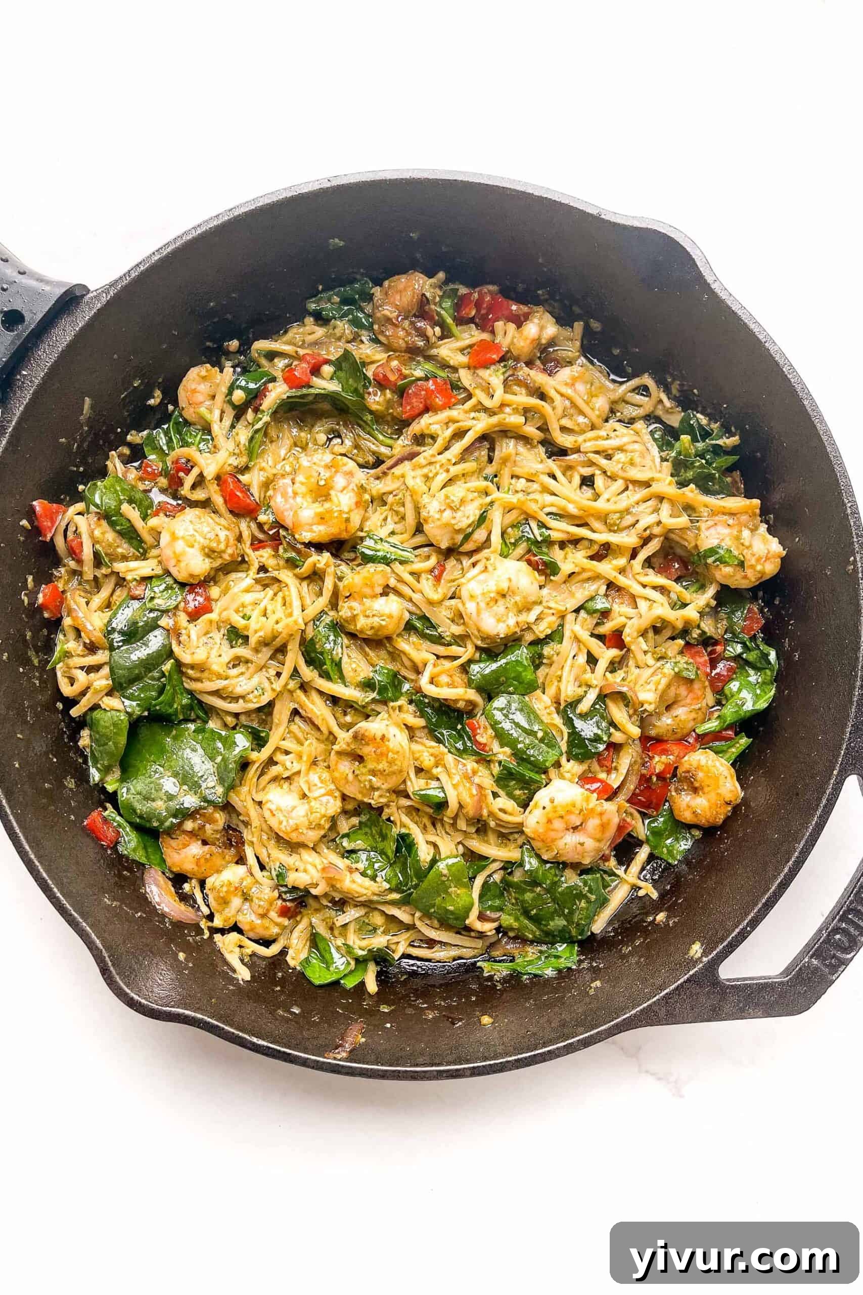 Close-up of creamy pesto shrimp pasta simmering in a cast iron skillet, showcasing the rich sauce and perfectly cooked ingredients.
