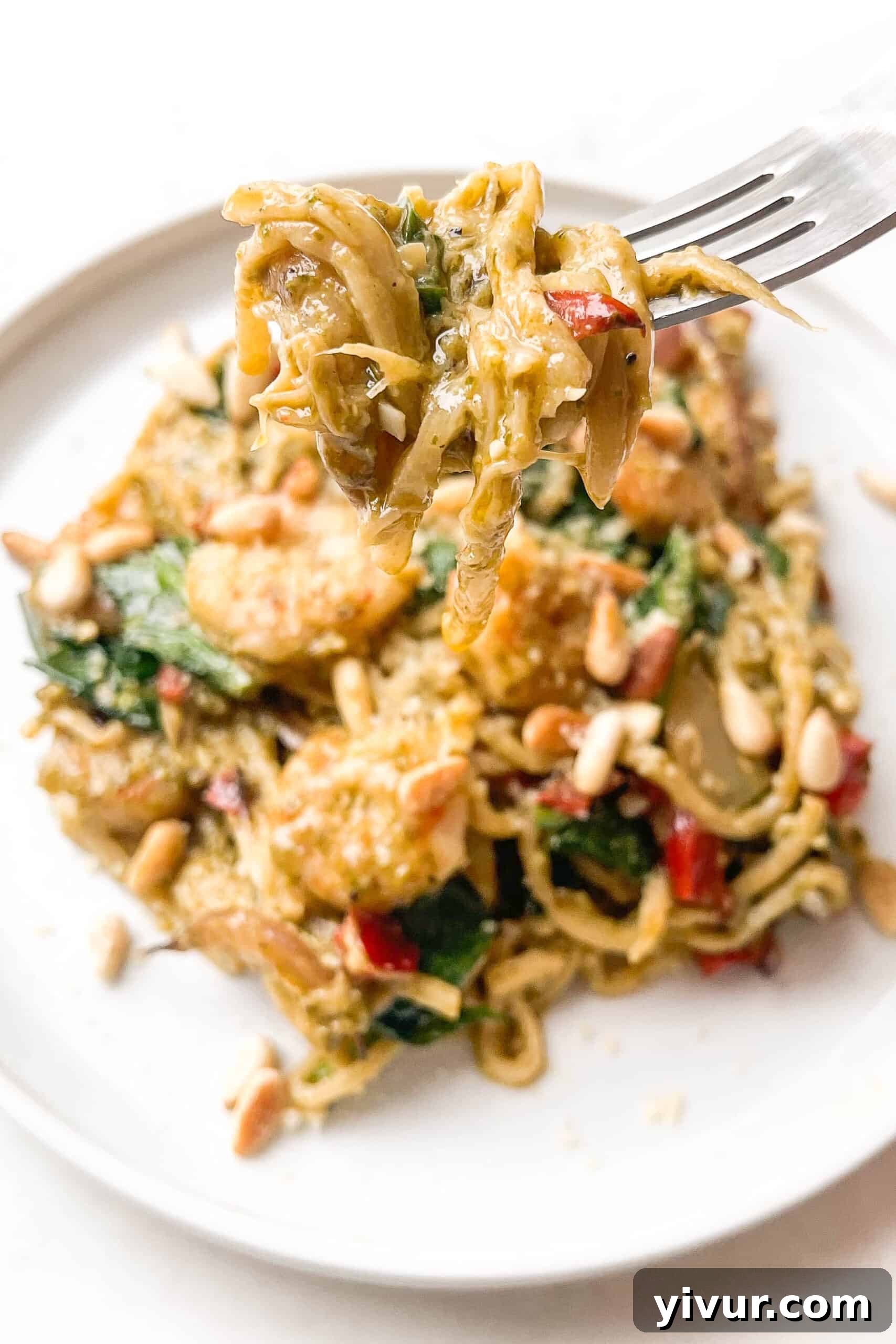 A close-up shot of the finished pesto shrimp pasta on a clean white plate, ready to be enjoyed, garnished with fresh basil and pine nuts.