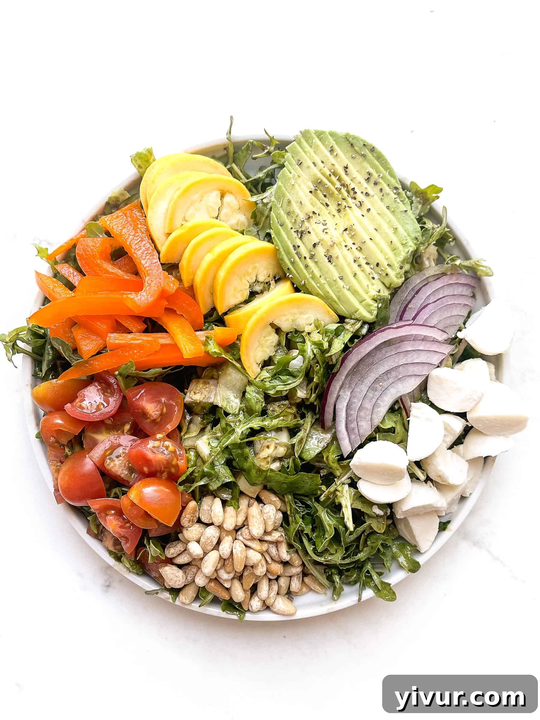 Close-up of the rainbow chopped salad, highlighting the vibrant colors and fresh textures of tomatoes, bell pepper, squash, avocado, red onion, mozzarella, and pinenuts nestled in a bed of arugula.