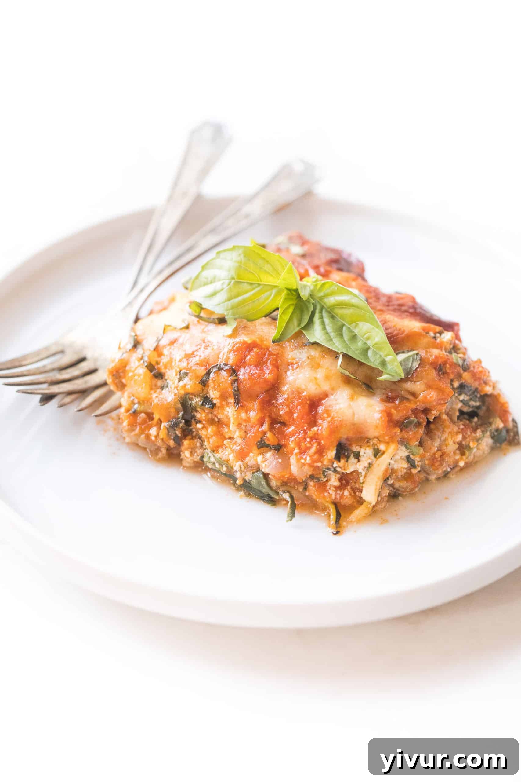Delicious keto low carb lasagna made with zucchini noodles on a white plate, showcasing beautiful layers of cheese, meat sauce, and fresh herbs.