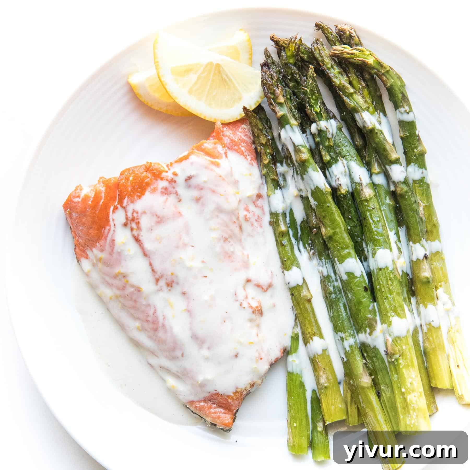 salmon with white sauce with lemon and asparagus on a white plate