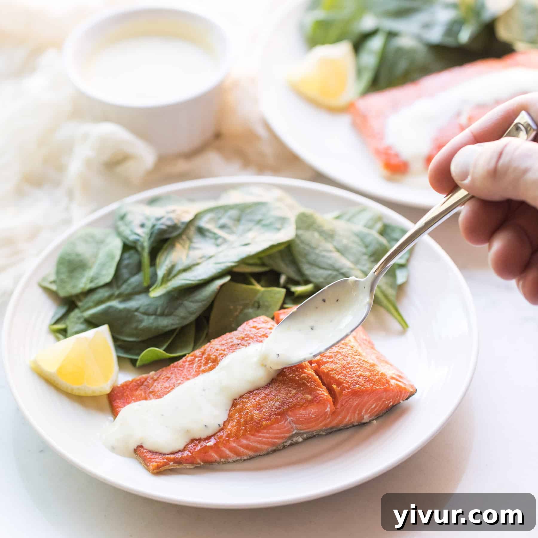 spinach and salmon on a white plate with a spoon drizzling sauce