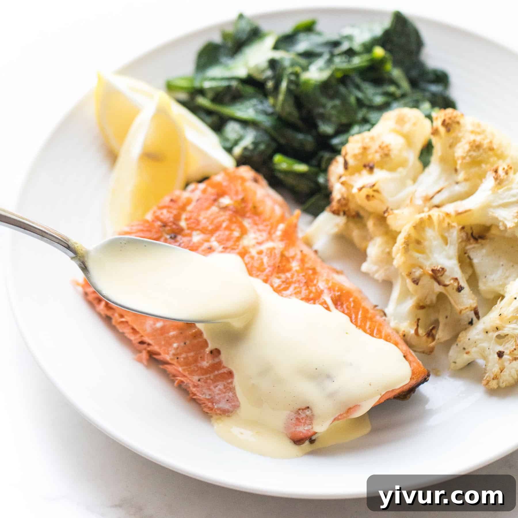 salmon with hollandaise sauce with roasted cauliflower and cooked spinach on a white plate