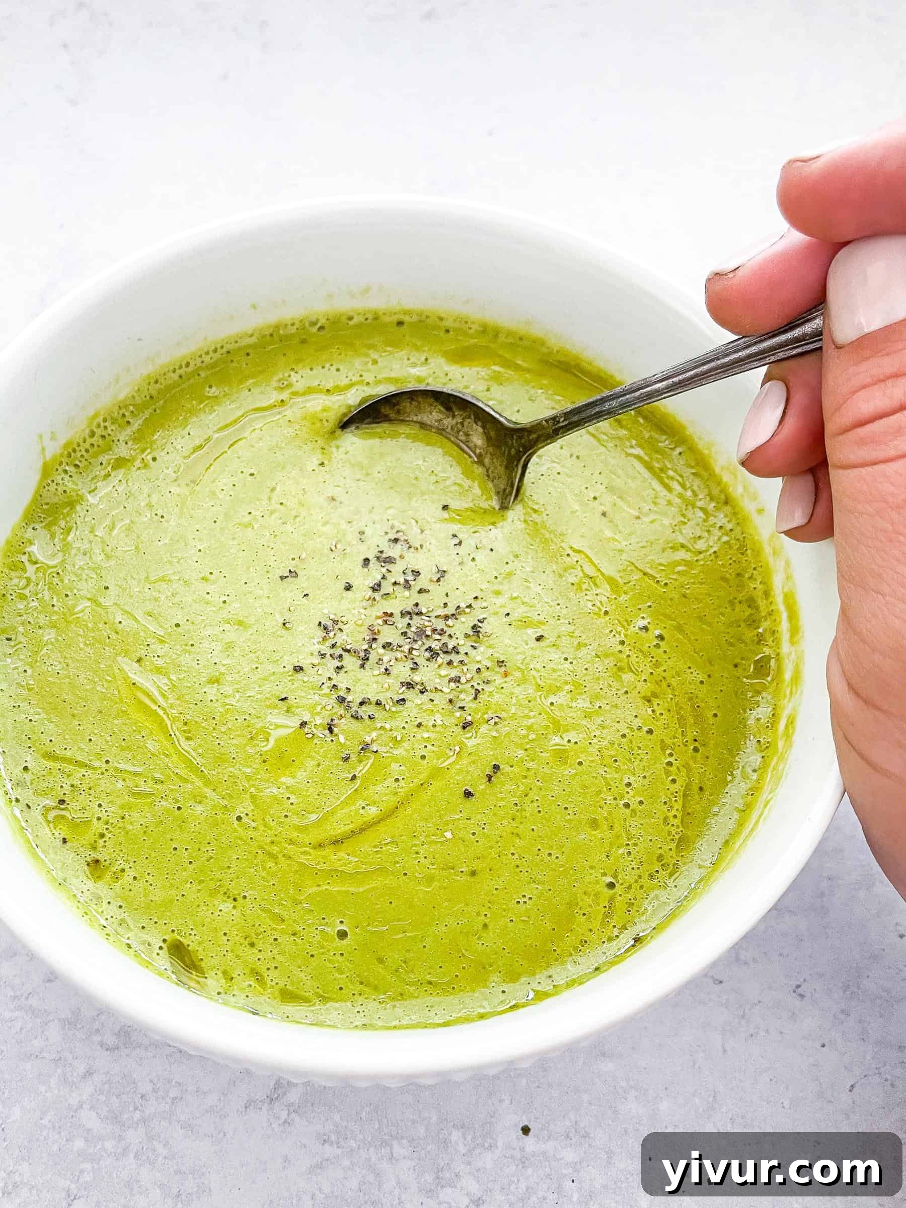 Close-up of a spoon dipping into a bowl of rich green cream of asparagus soup, highlighting its smooth texture and vibrant color.
