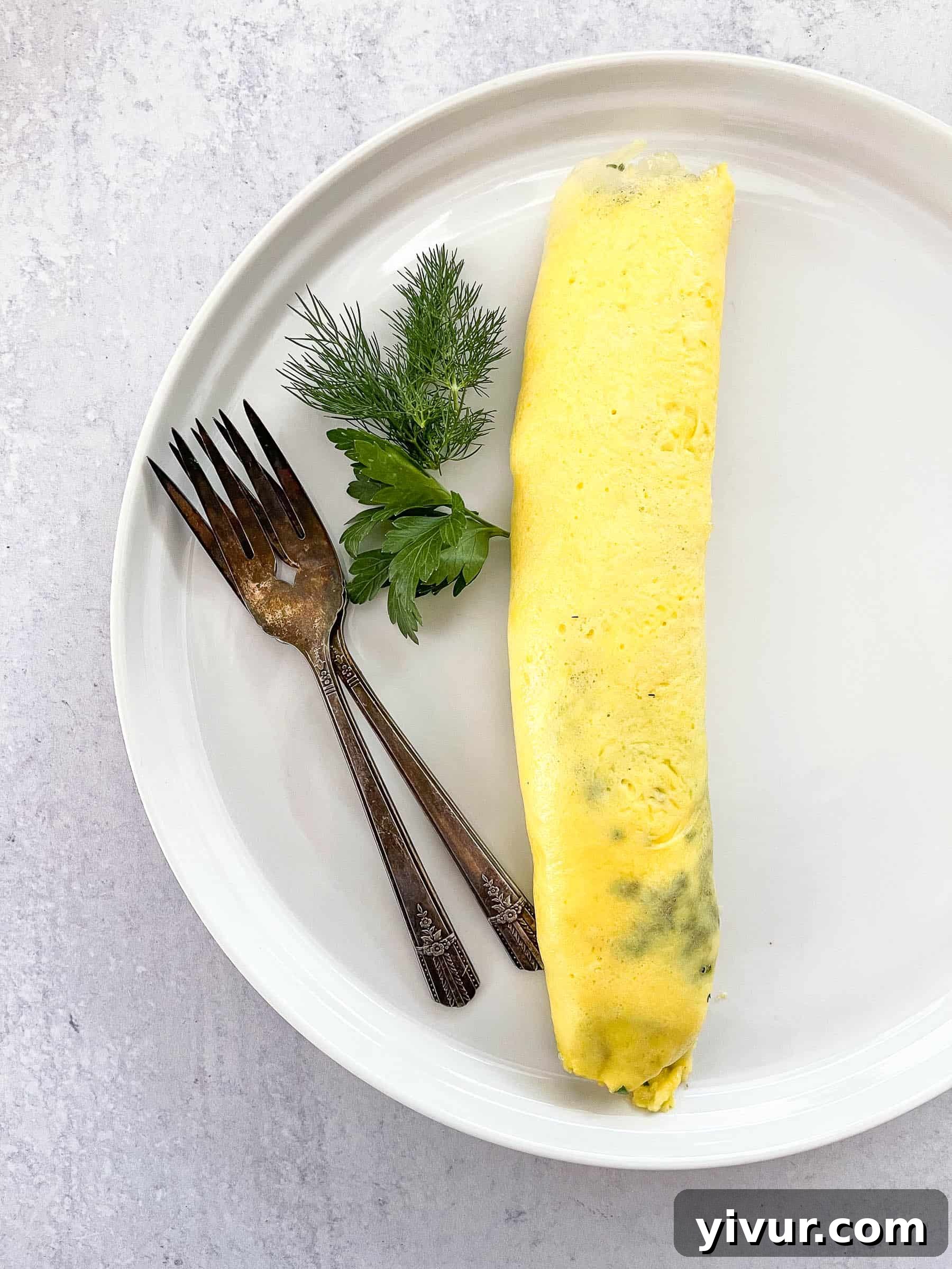 Classic Keto French Omelette on a white plate, garnished with vibrant fresh dill and parsley, presented with two antique forks.
