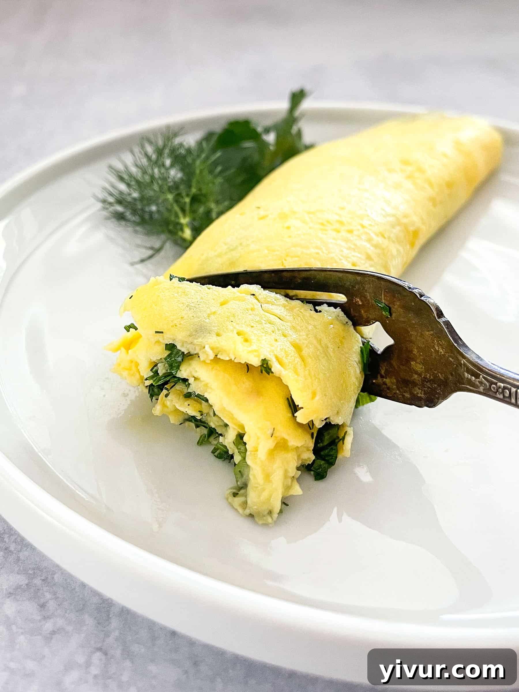 A beautifully cooked Keto French Omelette being gently cut with an antique fork, revealing its tender, fluffy interior, garnished with fresh herbs.