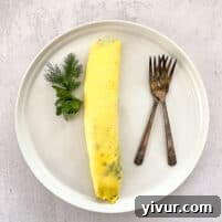 Beautifully plated Keto French Omelette garnished with fresh dill and parsley, ready to be served, capturing its exquisite presentation.