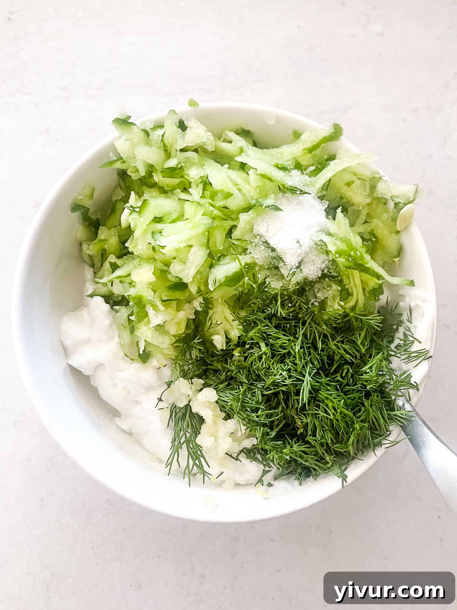 Creamy Keto Tzatziki Dip 3 Keto Tzatziki Sauce in a white bowl, next to fresh cucumber slices and dill sprigs.