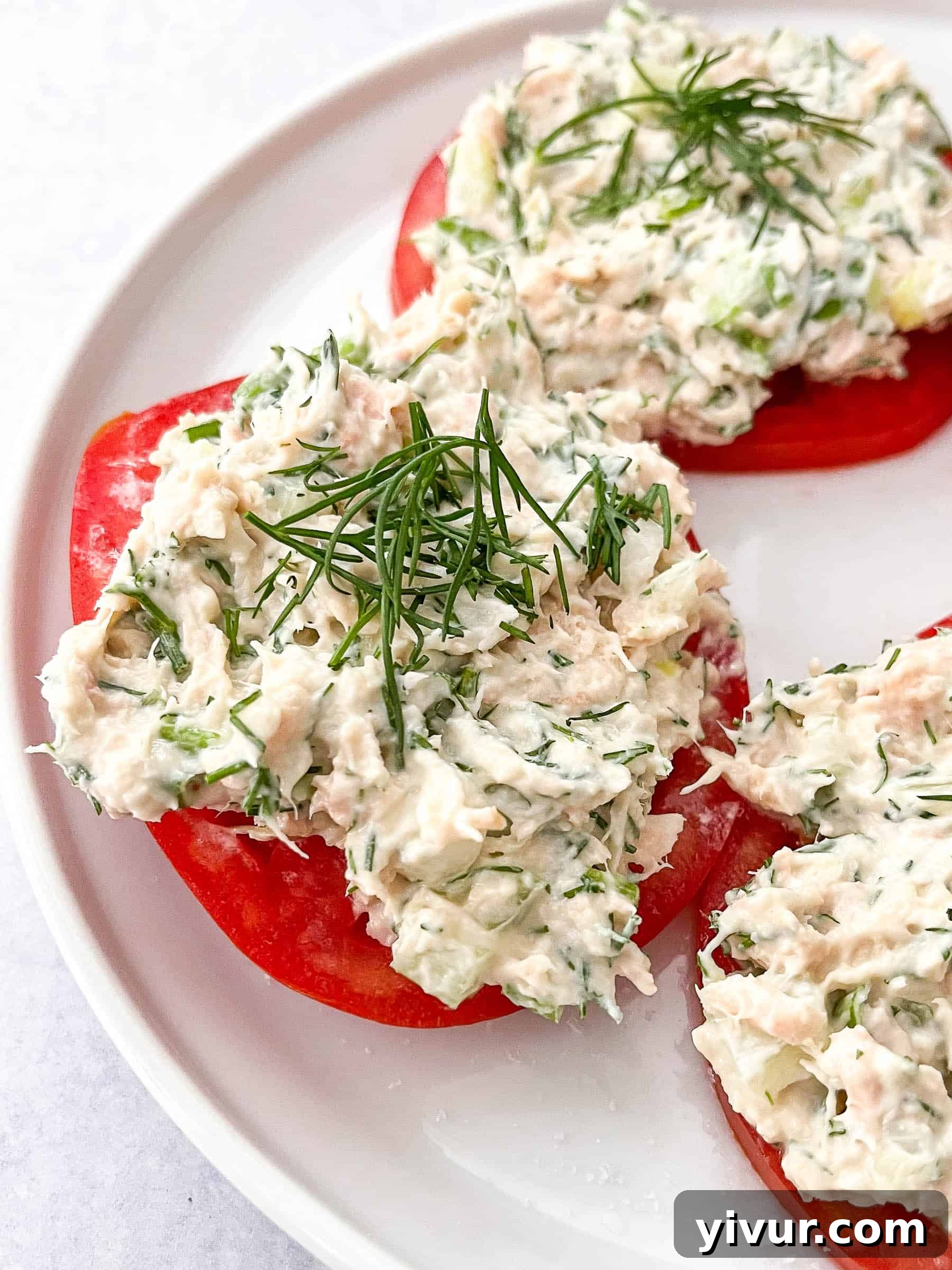Tuna salad topped with dill on sliced tomatoes on a white plate