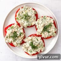 Tuna salad topped with dill on sliced tomatoes on a white plate