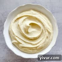 Dairy-free ricotta in a white bowl with a white background, garnished with fresh herbs.